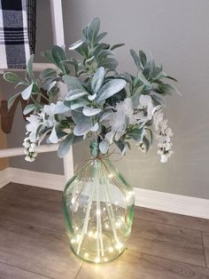 a vase filled with white flowers and greenery sitting on top of a wooden floor