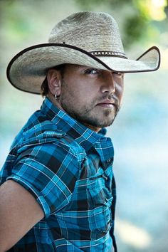 a man wearing a cowboy hat and plaid shirt looking at the camera with his hand on his hip