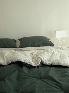 an unmade bed with green sheets and pillows on top of it, next to a night stand