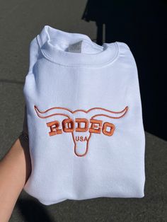 RODEO Cowboy Vintage sweatshirt! hold on tight! Western inspired crewneck! These sweatshirts and more are hand-made Each article made is locally crafted with heavy input from you! The sweatshirts and color of stitching can be picked according to your desires, and our advanced machine makes it possible to do almost any possible color combination. Kindly feel free to contact us at any time about any questions you might have!! Western Embroidered Sweatshirt, White Sweatshirt With Embroidered Graphics For Team Spirit, White Team Spirit Sweatshirt With Embroidered Graphics, Western Clothing For Women, Dress Rodeo Outfit, Country Girl Outfits, Western Crewneck, Cowboy Vintage, Western Sweatshirts