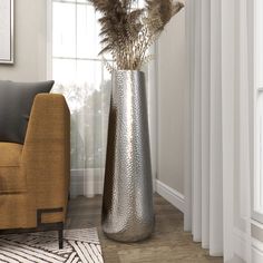 a tall metal vase sitting on top of a wooden floor next to a chair and window