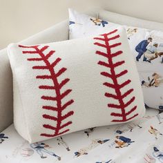 a baseball themed pillow on a bed with white sheets and pillows, along with red stitching