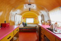 the interior of a small yellow and red bus with a bed, sink, stove, and refrigerator