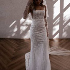 a woman in a white wedding dress standing on a wooden floor with her veil over her head