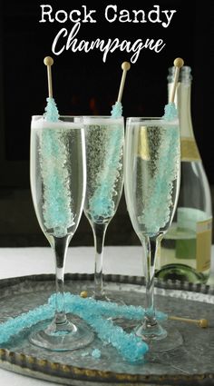 three champagne flutes with blue and green confetti in them on a tray next to bottles