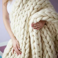 a woman is wrapped up in a giant chunky blanket, with her hands on the back