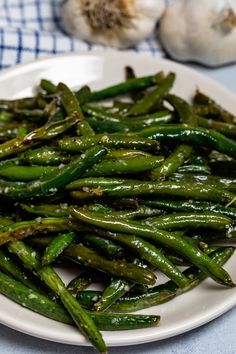 a white plate topped with green beans next to garlic