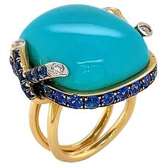 Striking blue of turquoise is the climax of this ring. The polished cabochon is bezel set in 18k yellow gold, which features two inter crossing diamond tipped strands on each side. Sapphires rotate in the bezel setting for a glimmering tranquil accent. Total weights for the gems are 0.14 carats of diamonds, 32.85 carats of turquoise and 3.12 carats of sapphire. The split band complements the setting for a bold finishing touch. Ruby Gold Ring, Yellow Gold Cocktail Ring, Alexis Bittar Jewelry, Cushion Cut Ring, Gold Cocktail Ring, Contemporary Ring, Blue Sapphire Diamond, Colombian Emeralds, Cabochon Ring