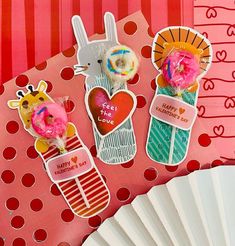 three valentine's day stickers sitting on top of a pink card board next to a fan