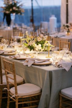 the table is set with white linens and gold place settings, along with flowers