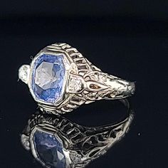 This vintage 18K white gold engagement ring features a stunning 1.64 carat cushion-cut blue sapphire gemstone, which is set in a bezel setting. The ring is also adorned with a diamond accent, making it a perfect choice for an engagement, anniversary, birthday, or even Mother's Day. The ring is sizable and comes with a certification from AGI, ensuring its authenticity. Gorgeous Vintage art deco filigree 18k white gold engagement ring blue sapphire in cushion shape circ 1920's center natural sapph Engagement Ring Blue Sapphire, Engagement Ring Blue, Ring Blue Sapphire, Art Deco Filigree, Blue Sapphire Gemstone, Sapphire Engagement Ring Blue, White Gold Engagement Ring, Ring Blue, Timeless Art