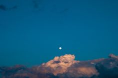 the moon is shining in the blue sky above some fluffy white clouds and dark, dreary clouds