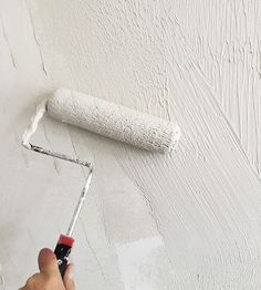 a person painting a wall with white paint and a roller in the middle of it