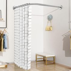 there is a white shower curtain in the bathroom with clothes hanging on racks and a mirror behind it