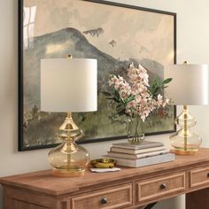 a table with two lamps and a painting on the wall behind it, along with some books