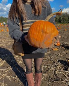 a woman holding a pumpkin in her hands and looking at the camera while wearing boots