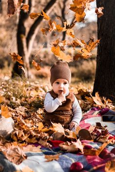 a baby sitting on a blanket in the leaves