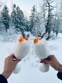 two people holding up wine glasses with oranges on them in front of snow covered trees