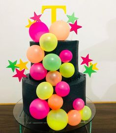 a three tiered black cake with stars and balloons on the top, sitting on a table