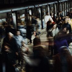 a crowd of people walking across a train station next to a loading platform at night