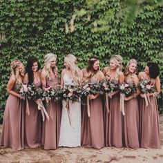 a group of women standing next to each other wearing dresses and holding bouquets in their hands