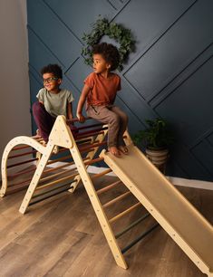 two children playing on a wooden slide in a room with blue walls and wood flooring