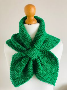 a green knitted scarf sitting on top of a white mannequin