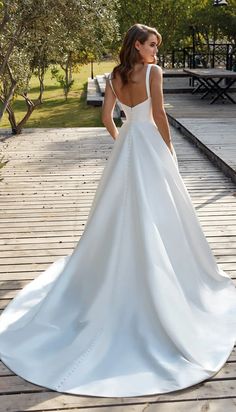 a woman in a white wedding dress is standing on a wooden deck with her back to the camera