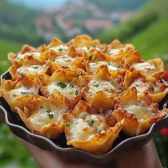 a person holding up a dish of food in their hand with mountains in the background