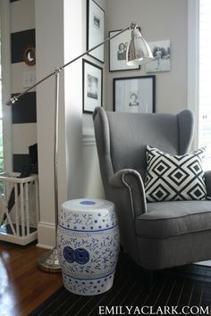 a living room with a gray chair and blue and white vase on the floor next to a lamp