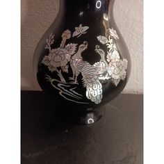 a black vase sitting on top of a table with flowers painted on the side of it