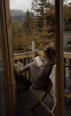 a woman sitting in a chair on top of a wooden deck next to a window