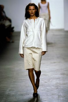 a woman walking down a runway wearing white clothes