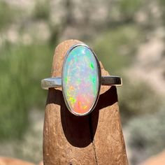 "This opal and silver ring features an oval 16.6 x 8.2 mm, 2.65 carat Ethiopian opal gemstone, set in an artisanal handmade silver bezel ring. We used fine silver for the bezel and American recycled Sterling Silver for the ring band and backplate. This stunning gemstone is milky translucent with confetti-like flashes of blue, green, yellow and red! Ethiopian opal can appear nearly clear or milky without flashes at certain angles or in low light. There are a few tiny pits on one side of the opal Oval Opal Rings With Polished Finish, Polished Opal Ring In Oval Cabochon Shape, Opal Oval Cabochon Ring With Polished Finish, Polished Opal Oval Cabochon Ring, Ethiopian Opal Oval Rings As Gifts, Oval Opal Cabochon Ring, Sterling Silver Oval Opal Cabochon Ring, Oval Cabochon Opal Ring In Sterling Silver, Oval Ethiopian Opal Ring For Anniversary