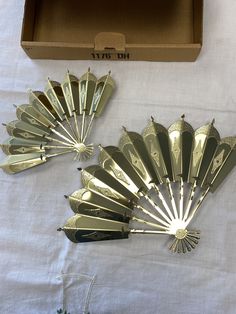 three gold fan shaped brooches sitting on top of a white cloth covered table