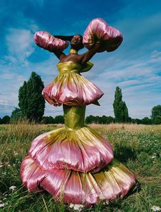 a woman in a dress made out of pink and yellow petals is standing in the grass