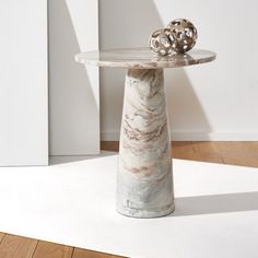 a marble table with a metal object on top in front of a white wall and wooden floor