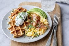 a white plate topped with waffles, eggs and avocado next to a fork