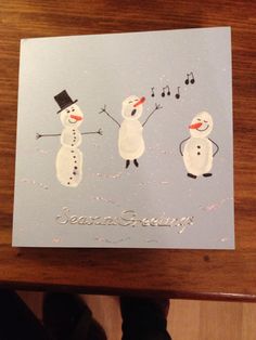 someone is holding up a christmas card with two snowmen on it and music notes in the background