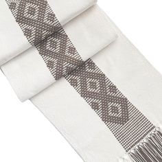 a white scarf with grey and white designs on the border, folded in two rows