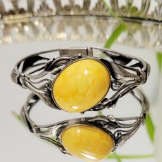 Vintage Art Nouveau 1900s Egg Yolk Amber bracelet! Unmarked intricate lily detailed bracelet that seems to be comprised of sterling silver and Egg yolk amber (possibly Baltic). Absolutely STUNNING rare treasure of a piece in spectacular condition, only minor tarnish on the metal, the face of the amber cabochon has no scratches. .7 oz. Elegant Sterling Silver Cabochon Bracelet, Vintage Bangle With Polished Finish, Silver Cabochon Bracelet For Wedding, Elegant Amber Bangle Jewelry, Wedding Silver Bracelet With Cabochon, Vintage Amber Engraved Jewelry, Vintage Amber Jewelry With Engraved Details, Vintage Yellow Cabochon Jewelry, Vintage Yellow Jewelry With Cabochon