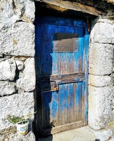 an old blue door is open on a stone building with a potted plant next to it