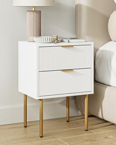 a white bedside table with two drawers and a lamp on the nightstand next to it