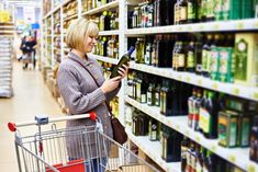 a woman shopping in a grocery store looking at the shelves with drinks on it and holding a tablet