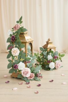 two small lanterns with flowers and greenery on the floor next to eachother