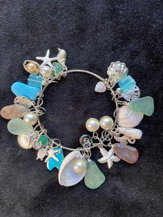 "Kingman Turquoise Ocean Jasper Sea shells beach glass Pearls and Sterling plated beach charms on a bangle charm bracelet. With Ocean Jasper, 6 Pearls, 2 Sea shells, 6 pieces of beach glass, 12 beach charms, 3 hand blown glass beads, 1 Petoskey stone, a piece of Kingman Turquoise and 2 blue glass beads finish this bangle charm bracelet.   The bangle bracelet is  2.5\" inches in width. See all my charm bracelets here: https://www.etsy.com/shop/MoonwaterJewelryShop?section_id=34394213 All my bracelets are different and would be considered one of a kind. View my collection of Kingman Arizona Turquoise here: https://www.etsy.com/shop/MoonwaterJewelryShop?section_id=28192591  I've been selling on eBay since 2003 Came to Etsy to sell jewelry. Returns and exchange details ► RETURNS / EXCHANGES Al Shell Charm Bracelet, Beach Glass Nails, Sea Glass Bangle, Beach Charms Bracelet Jewelry, Bohemian Beach Bracelets With Charms, Bohemian Charm Bracelets For The Beach, Beach Ocean-inspired Charm Bracelet, Handmade Charm Bangle For Beach, Handmade Dangle Bracelets For Beach