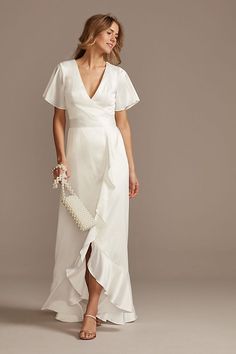 a woman wearing a white dress with ruffles on the side and a clutch in her hand