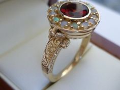 This majestic Vintage Garnet & Opal ring has been crafted with reference to a Victorian design from 9ct/9k Solid Yellow Gold.  A NATURAL Garnet has been bezel set in the centre surrounded with prong set NATURAL Fiery Opals.   Beautifully decorated Acanthus Leaves and Filigree Patterns adorn the shoulders adding additional appeal to this feminine ring.  The highlight for this exotic ring is a custom crafted lid can be opened to place secret contents inside. THIS VINTAGE INSPIRED GARNET & OPAL RIN Garnet Ring Vintage, Opal Ring Vintage, Womens Ring, Opal Ring Gold, Ring Antique, Classy Jewelry, Garnet Ring, Garnet Rings, Opal Ring