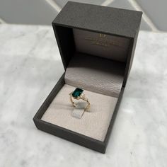 an open box with a ring in it sitting on a counter top next to a white marble floor