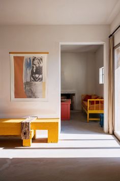 an empty room with yellow benches and pictures on the wall above them, in front of a sliding glass door